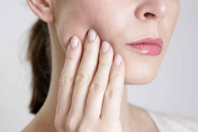 woman holds cheek in tooth pain